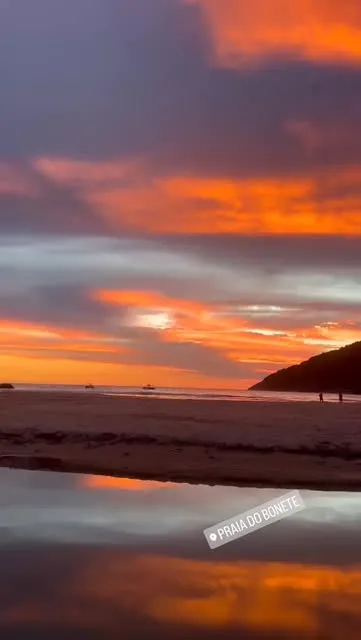 Pôr do sol alaranjado refletido na areia molhada da Praia do Bonete
