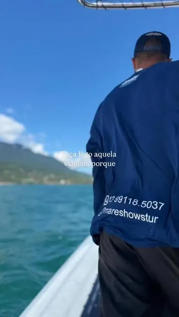Piloto da Maré Show na proa da lancha, de frente para o mar e a serra de Ilhabela